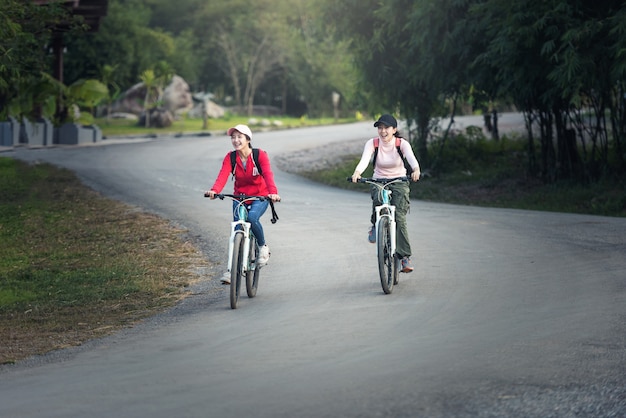 Zwei stilvolle junge Freundinnen auf einem Fahrrad entlang der Straße. Beste Freunde, die einen Tag auf dem Fahrrad genießen.