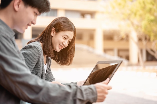 Zwei Studenten, die das Buch lesen und per Laptop an der Treppe in der Universität lernen.