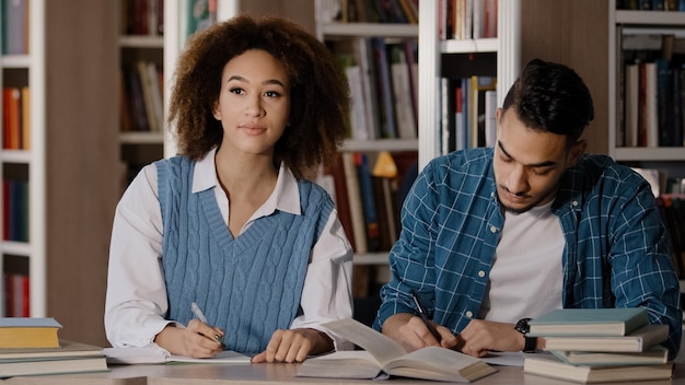 Zwei Studenten, junger Mann und Mädchen, die Hausaufgaben machen, sitzen am Schreibtisch in der Bibliothek und schreiben aufmerksam Notizen