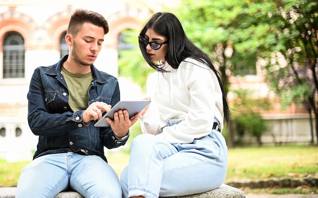 Zwei Studenten lernen zusammen mit einem digitalen Tablet, das auf einer Bank im Freien sitzt