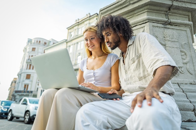 Zwei Studenten nutzen beim Lernen gemeinsam einen Laptop, während sie in der Stadt sitzen