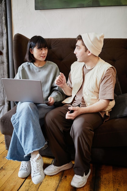 Zwei Studenten sitzen auf dem Sofa mit Laptop und diskutieren gemeinsam im Raum über Online-Bildung