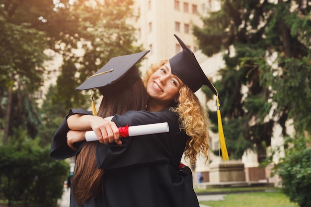 Zwei Studenten umarmen sich an ihrem Abschlusstag an der Universität, haben Spaß und verabschieden sich von einem Freund. Bildungs-, Qualifikations- und Kleiderkonzept.