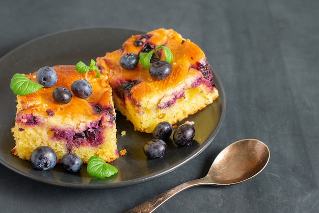 Zwei Stücke Blaubeerkuchen auf einer dunklen Untertasse.