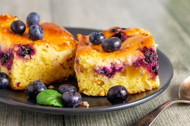 Zwei Stücke Blaubeerkuchen auf einer dunklen Untertasse.