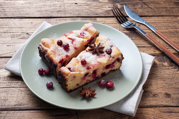 Zwei Stücke Hüttenkäse-Tortenkasserolle mit Moosbeerbeeren und Gewürzzimt und -anis auf einer Platte.