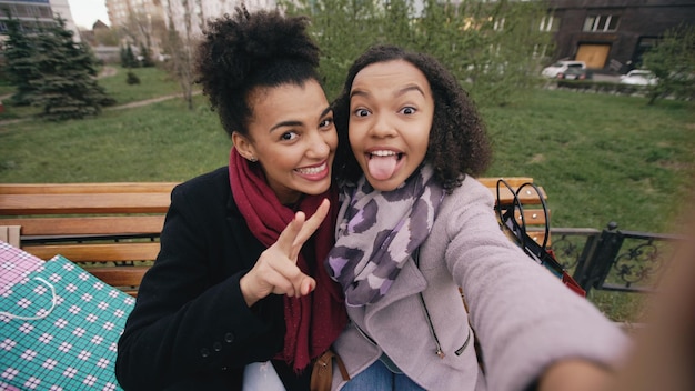 Foto zwei süße afroamerikanerinnen, die mit einkaufstüten ein selfie auf dem smartphone machen und lächeln