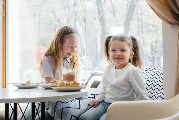 Zwei süße kleine Mädchen sitzen in einem Café und spielen an einem sonnigen Tag. Erholung und Lebensstil.