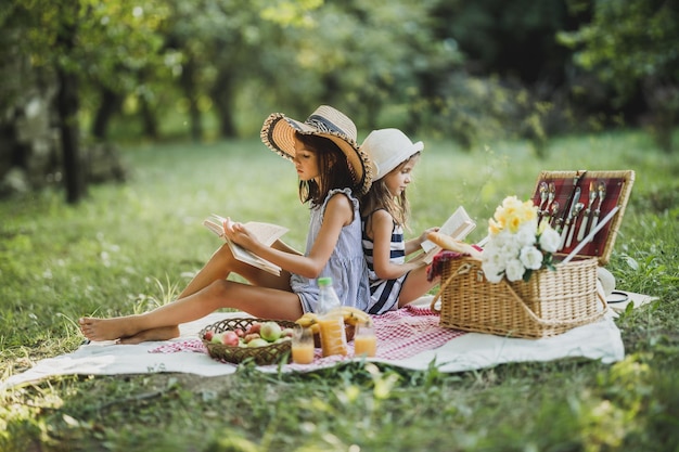 Zwei süße Schwestern lesen Bücher in der Natur und genießen einen Picknicktag.