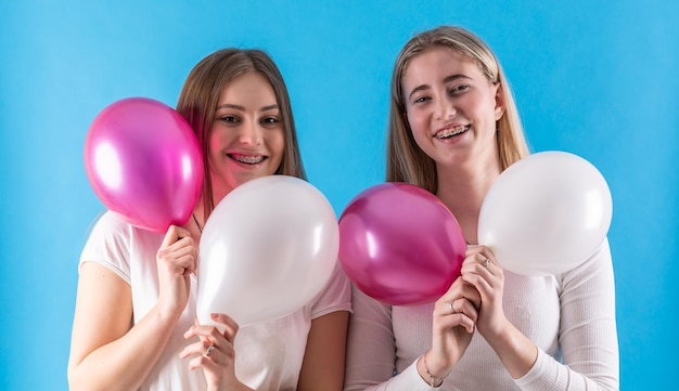 Zwei süße Teenager mit Zahnspangen und Luftballons vor blauem Hintergrund