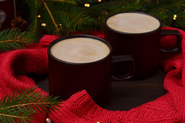 Zwei Tassen Cappuccino auf dem Tisch Nahaufnahme roter Pullover und Weihnachtsbaum