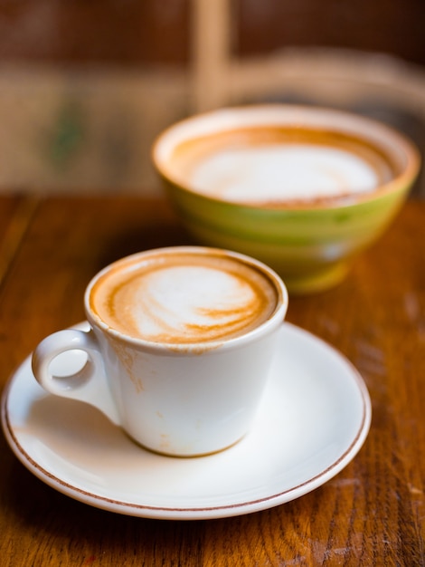 Zwei Tassen Cappuccino mit Latte Art auf Holzhintergrund. Konzept des einfachen Frühstücks. Kleine und große Keramiktassen