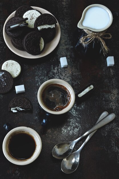 Zwei Tassen Espresso, ein Krug Milch und Schokoladenkekse mit weißer Füllung.