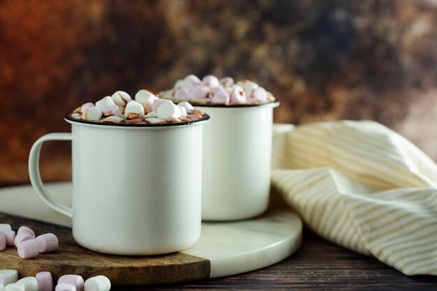 Zwei Tassen heiße Schokolade, Kakao oder warmes Getränk mit Marshmallows und süßen Keksen auf dunkel