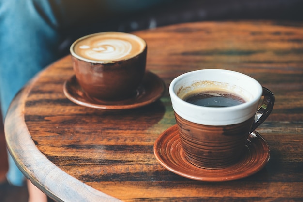 zwei Tassen heißen Latte-Kaffee und schwarzen Kaffee auf Vintage-Holztisch im Café