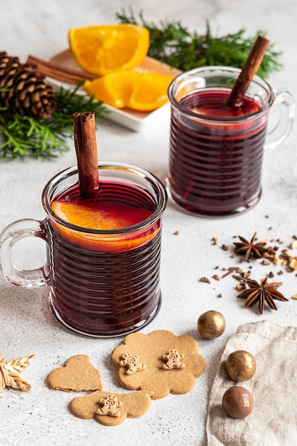 Zwei Tassen heißer Glühwein mit Zimtstangen und Orange. Gewürze, Ingwerplätzchen. Grauer Beton