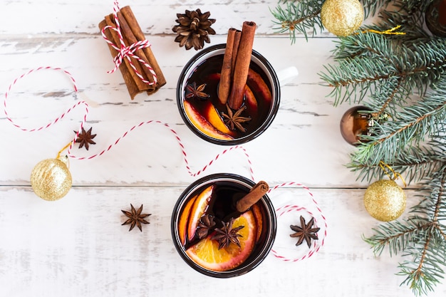 Zwei tassen herbstglühwein oder glühwein mit gewürzen und orangenscheiben auf rustikaler tischansicht. traditionelles getränk im herbst und winterurlaub.