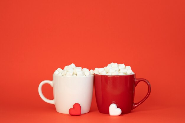 Zwei Tassen weiße und rote Farben mit Kakao und Marshmallows. Valentinstag oder Liebeskonzept.