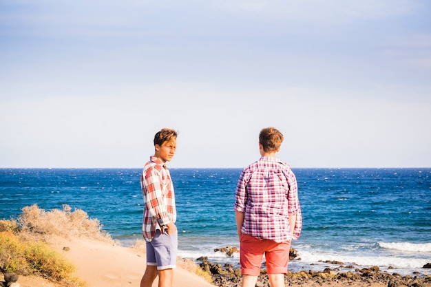 Zwei Teenager allein am Strand und isoliert auf das Meer schauen und miteinander reden - Erwachsene vor dem Meer, die Spaß haben und sich auf das Surfen vorbereiten