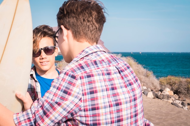 Zwei Teenager am Strand mit einem Surftisch, die miteinander reden und Spaß haben - Urlaub am Meer Lifestyle-Konzept