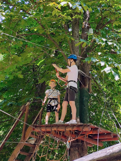 Zwei Teenager stehen auf einer Holzpalette an einem Baum in einem Seilpark in einem Sicherheitsgurt