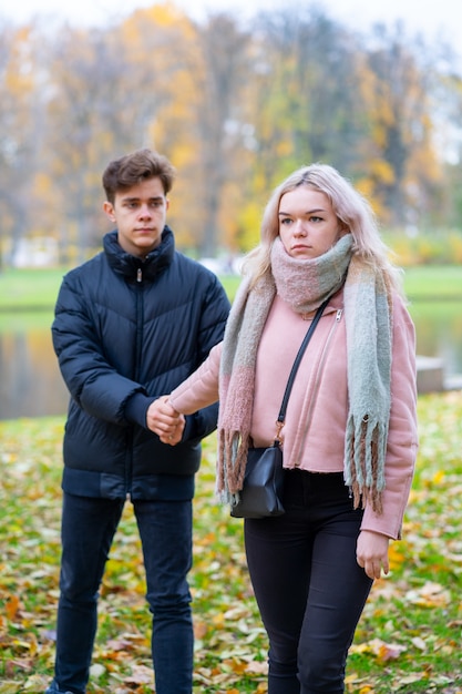 Zwei Teenager verliebt in Streit. Das blonde Mädchen ärgert sich über Jungen, Kerl hält ihre Hand,