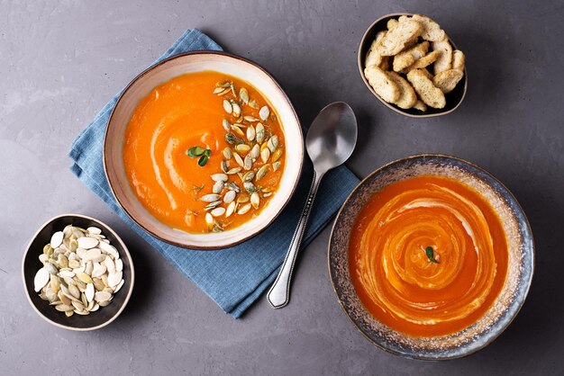 Zwei Teller vegetarische Kürbiscremesuppe auf grauem Hintergrund.