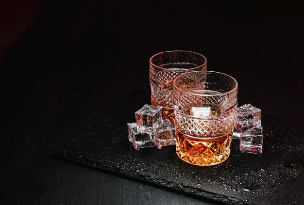 Zwei teure Gläser Whisky mit Eis auf einem schwarzen Steintablett