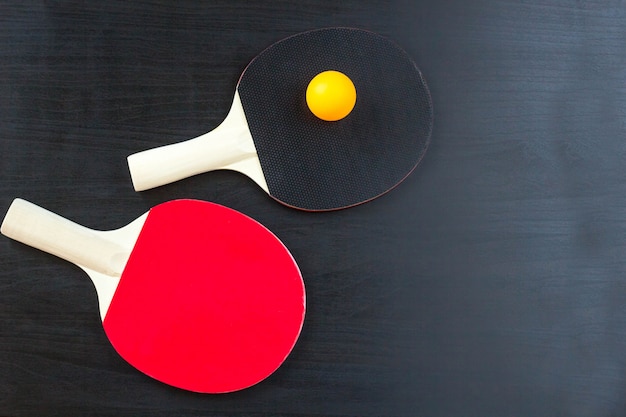 Zwei Tischtennis- oder Tischtennisschläger und Ball auf einem schwarzen Hintergrund