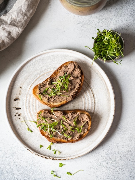 Zwei toasthuhn rillettes (pastete) auf weißbrot mit sprösslingen auf weißer platte auf einem licht. ansicht von oben