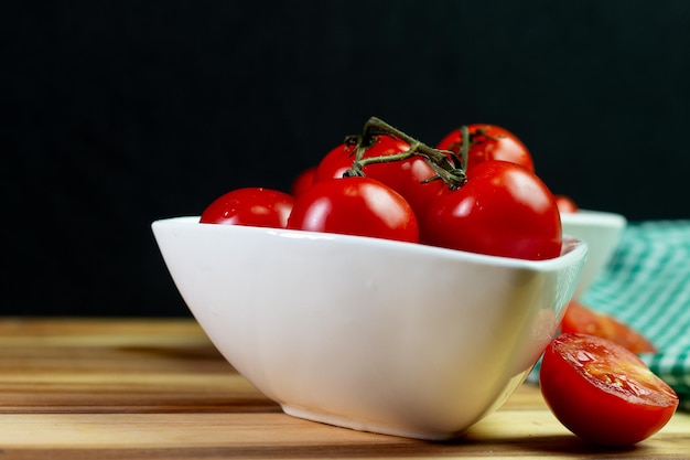 Zwei Tomatensorten in einer weißen Schüssel auf einem Holztisch mit schwarzem Hintergrund