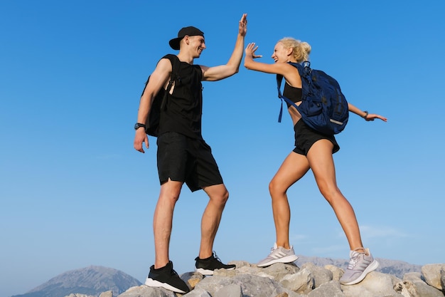 Zwei Touristen geben sich während der Feier des Bergsteigens ein High Five Hintergrund des blauen Himmels und der Berge im Sommer