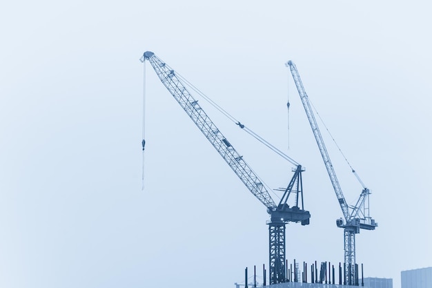 Zwei Turmkranen auf einer Baustelle unter bewölktem Himmel