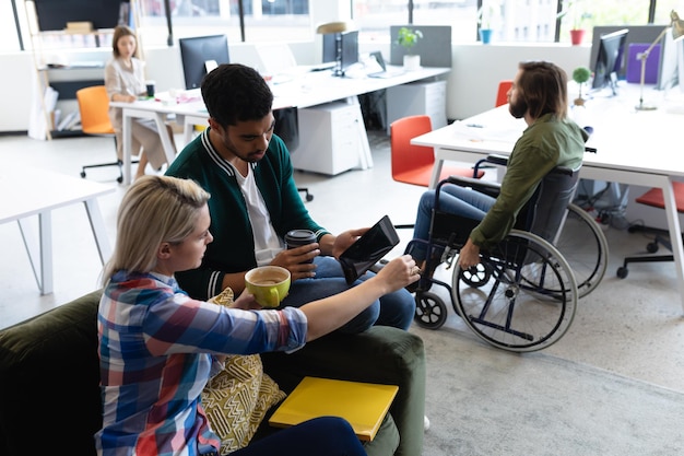 Zwei unterschiedliche Geschäftsleute, die im Kreativbüro arbeiten. Mann und Frau sitzen auf dem Sofa, trinken Kaffee und diskutieren über Arbeit. Geschäftsleute und Arbeitskollegen in einem geschäftigen Kreativbüro.