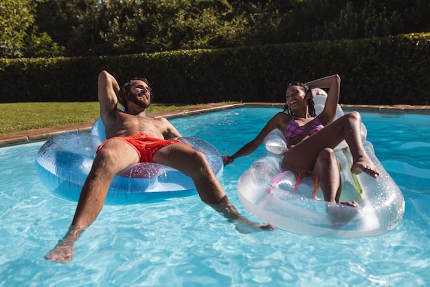 Zwei unterschiedliche männliche und weibliche Freunde haben Spaß beim Spielen auf Schlauchbooten im Schwimmbad. Im Sommer draußen abhängen und entspannen.