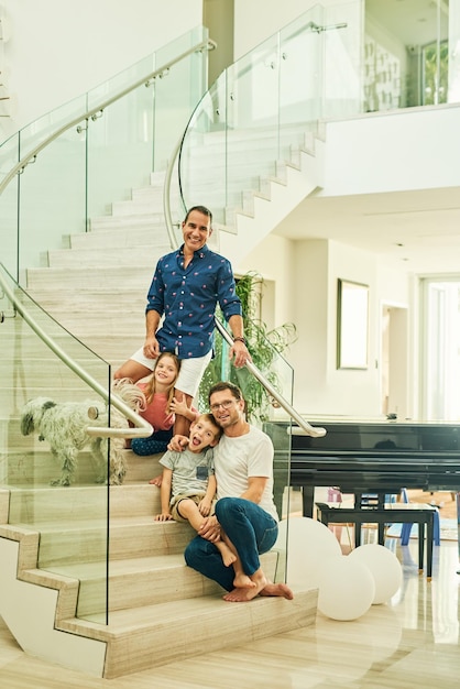 Zwei Väter sind besser als einer Ganzkörperporträt einer liebevollen vierköpfigen Familie auf der Treppe zu Hause