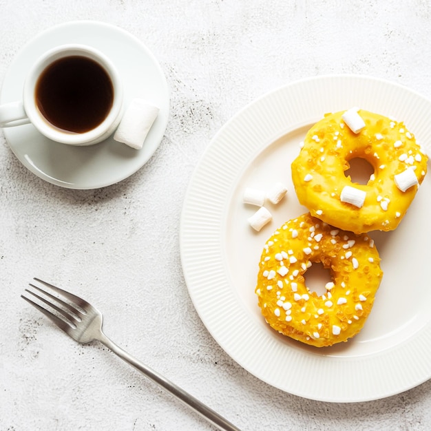 Zwei verglaste gelbe Donuts mit Marshmallows und einer Tasse Kaffee Serviert Frühstück oder Snack Draufsicht