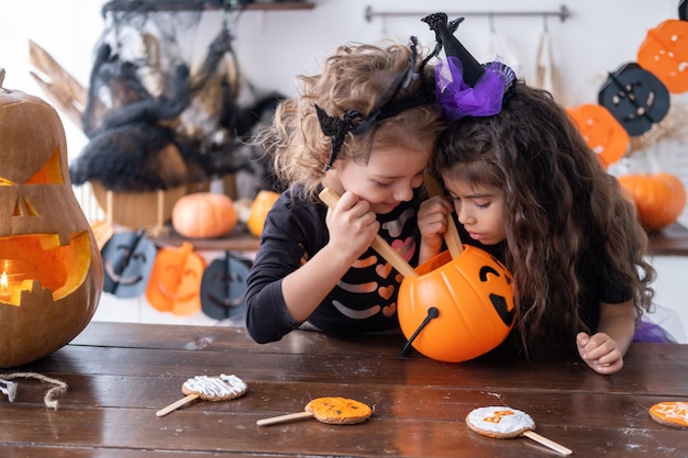 Zwei verschiedene Kindermädchen im Kostüm der Hexe, die sich zu Hause in der Küche amüsieren und Halloween feiern.