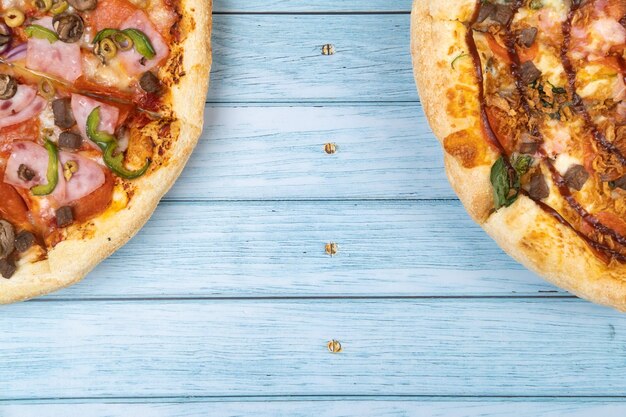 Zwei verschiedene leckere große Pizzen auf blauem Holzhintergrund.