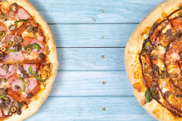 Zwei verschiedene leckere große Pizzen auf blauem Holzhintergrund.