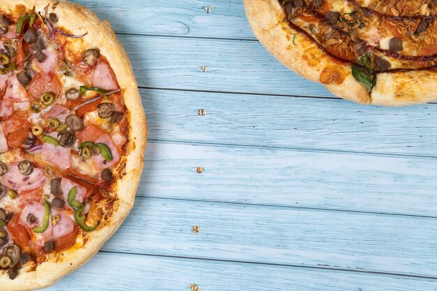 Zwei verschiedene leckere große Pizzen auf blauem Holzhintergrund.