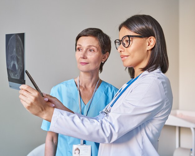 Zwei verschiedene Ärztinnen in Uniform, die sich die Hirntomographie ansehen und die Diagnose diskutieren