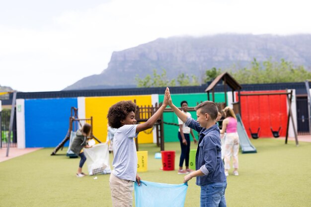 Zwei verschiedene Schuljungen sammeln Müll für das Recycling Highfiving auf dem Schulhof mit Kopierplatz