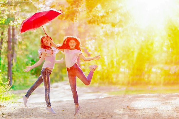 Zwei verspielte Mädchen mit einem roten Regenschirm für einen Spaziergang im Sommerwald Heller sonniger Tag