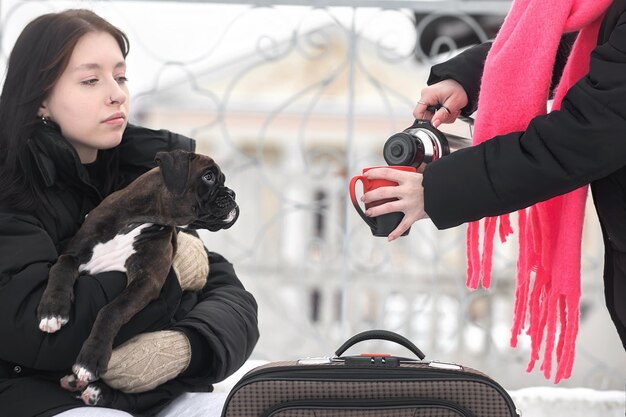 Zwei weibliche Reisende mit einem Hund trinken an einem Wintertag ein heißes Getränk aus einer Thermoskanne