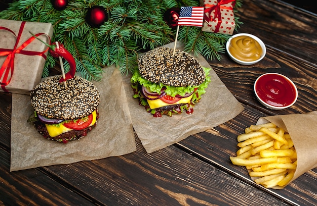 Zwei weihnachtliche schwarze Hamburger mit amerikanischem Schwarz, Salat, Tomate und Pommes Frites. Holzhintergrund