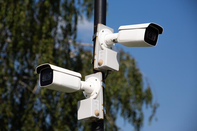 Zwei weiße Überwachungskameras an einer Stange schauen in verschiedene Richtungen für die Sicherheit auf einer Stadtstraße