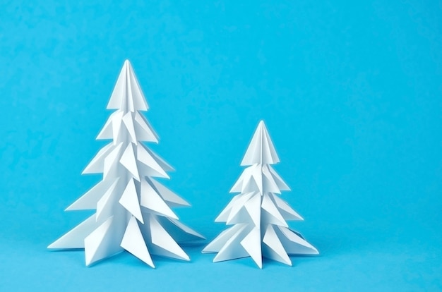 Zwei weiße Papierorigami-Weihnachtsbäume auf Blau