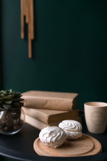 Zwei weiße schöne köstliche Marshmallows liegen auf dem Tisch neben einer Tasse Kaffee und Büchern auf dem Tisch. Foto in hoher Qualität