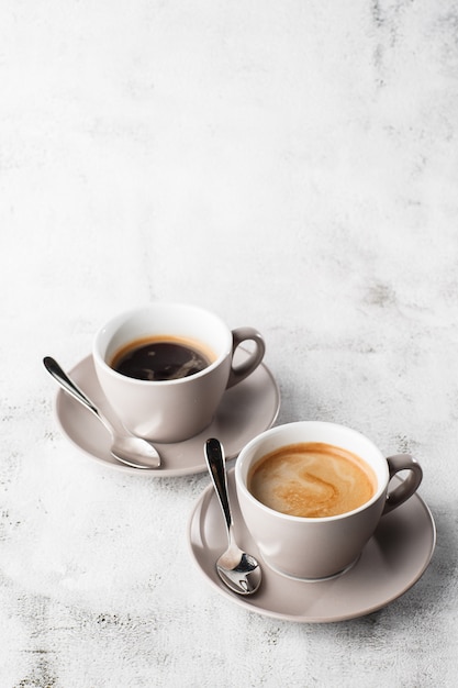 Zwei weiße Tassen heißen schwarzen Kaffees mit Milch lokalisiert auf hellem Marmorhintergrund. Draufsicht, Speicherplatz kopieren. Werbung für Cafe-Menü. Coffeeshop-Menü. Vertikales Foto.